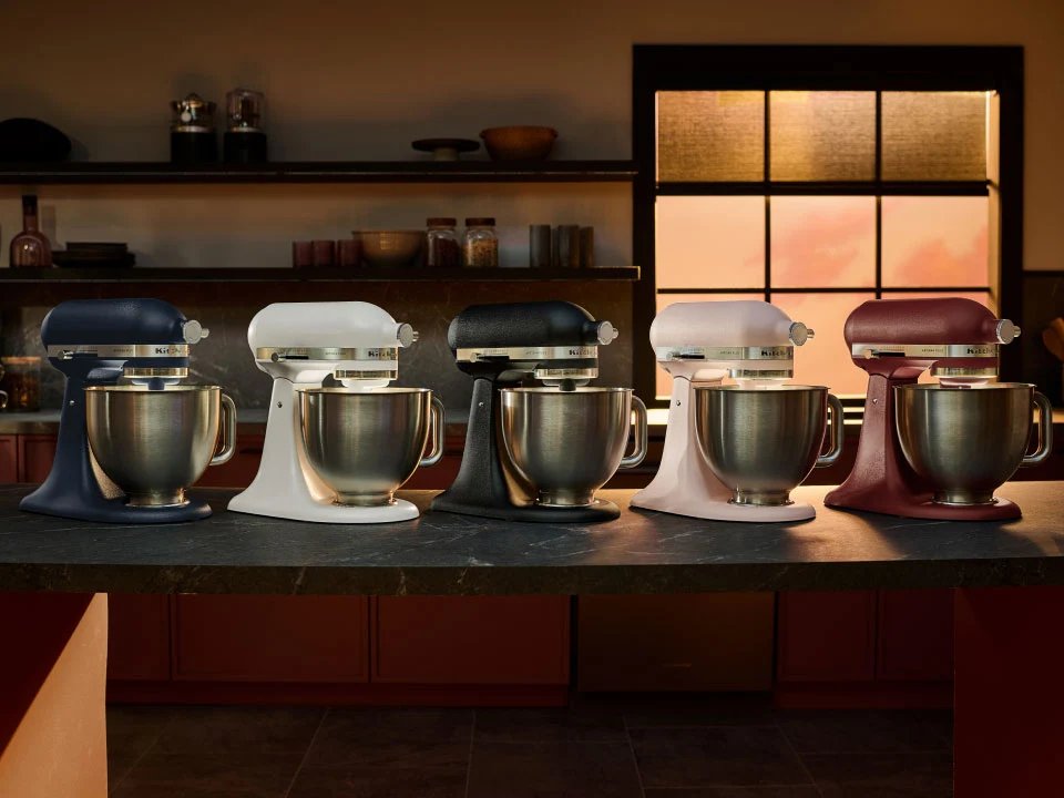 KitchenAid Artisan Plus stand mixers in a range of colours lined up on a kitchen bench